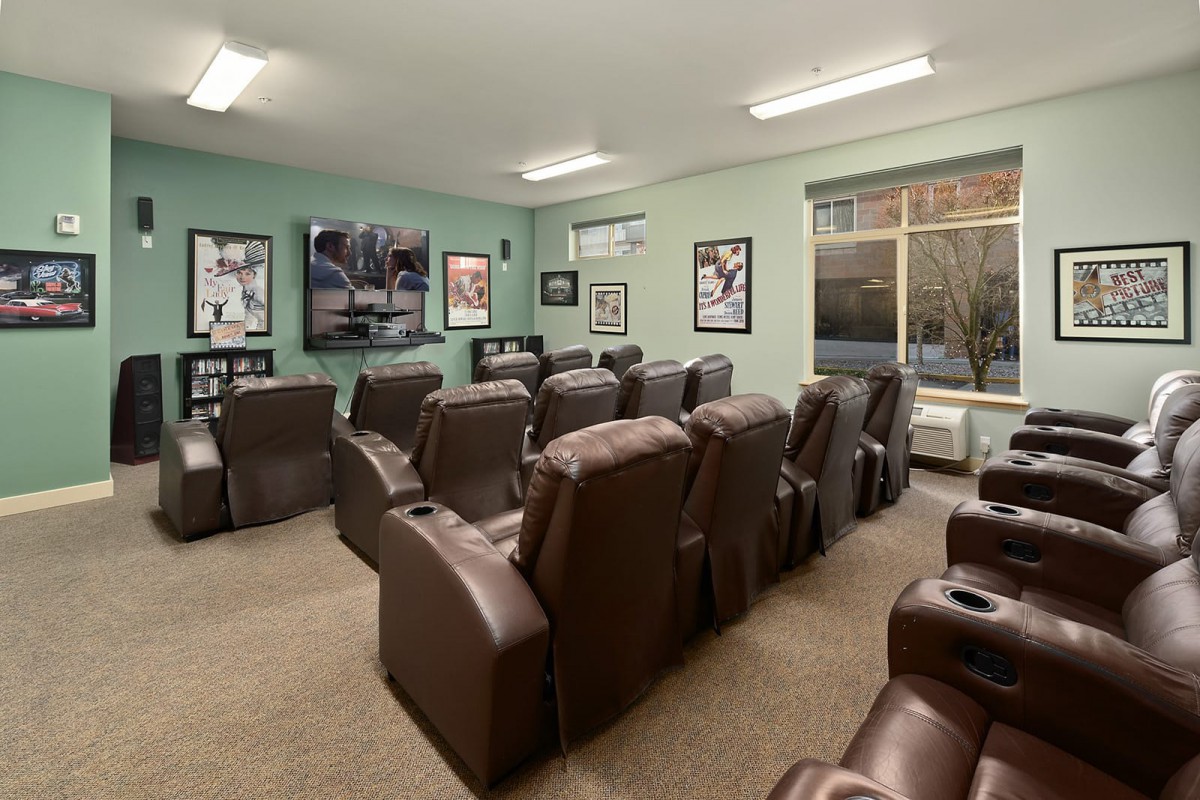 A cozy home theater room with multiple recliner chairs facing a large television, surrounded by movie posters on green walls.