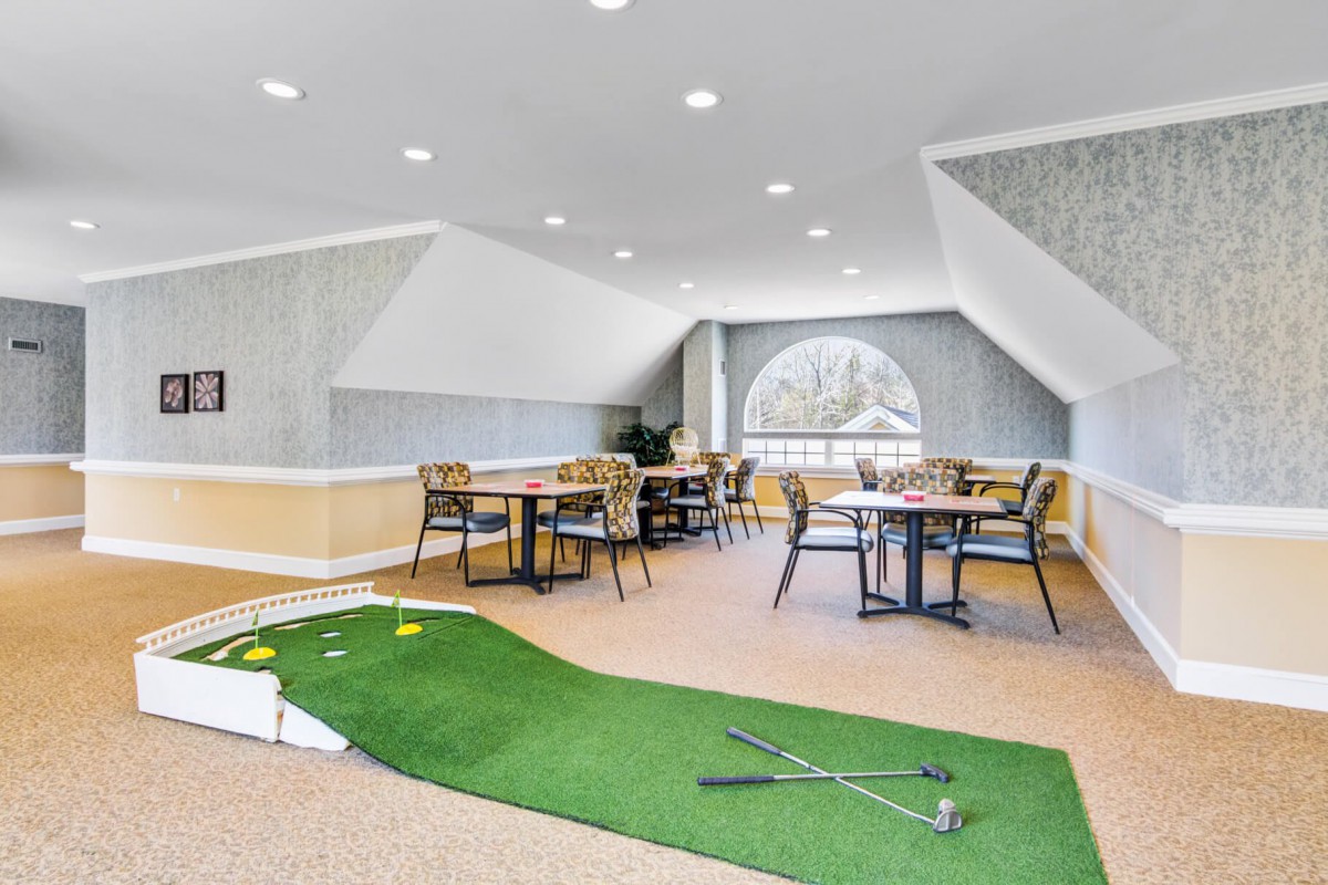 An indoor recreational space featuring a putting green and dining tables.