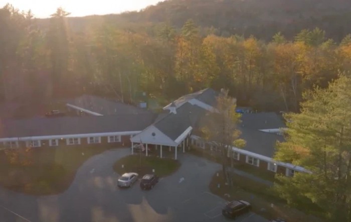 Aerial view of a building surrounded by autumn trees and sunlight.