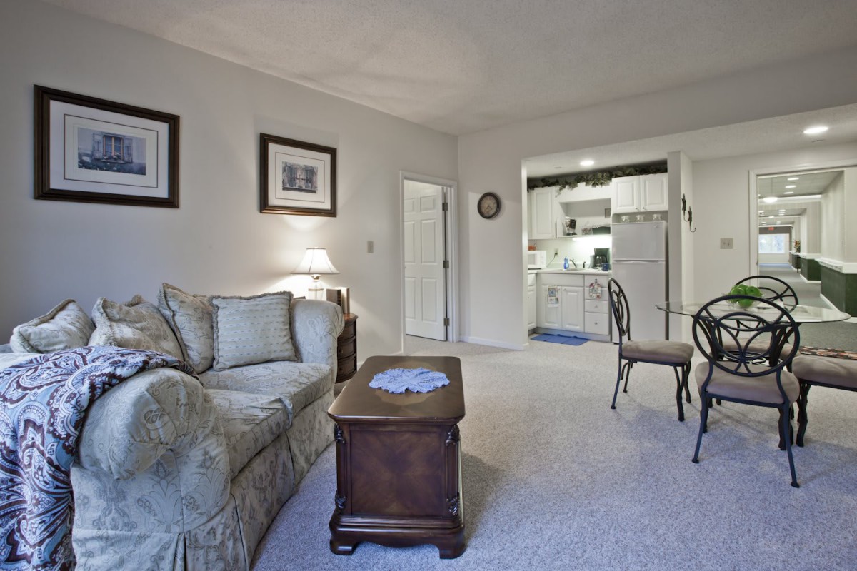 A cozy living room with a sofa, coffee table, and a view into the kitchen area.
