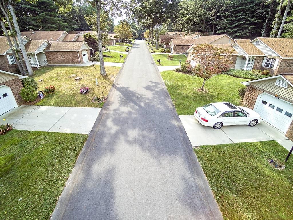 An aerial view of a quiet suburban neighborhood with houses lining the street and neatly maintained lawns.