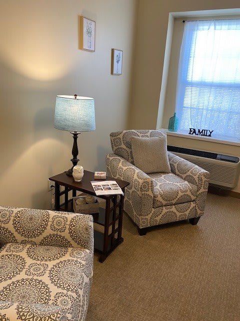 A cozy living room corner featuring patterned armchairs and a lit lamp on a wooden table.