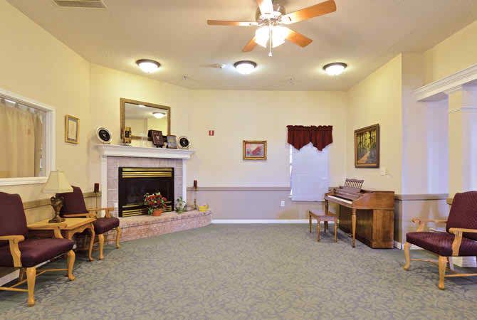 A cozy living room with a fireplace, ceiling fan, and piano.