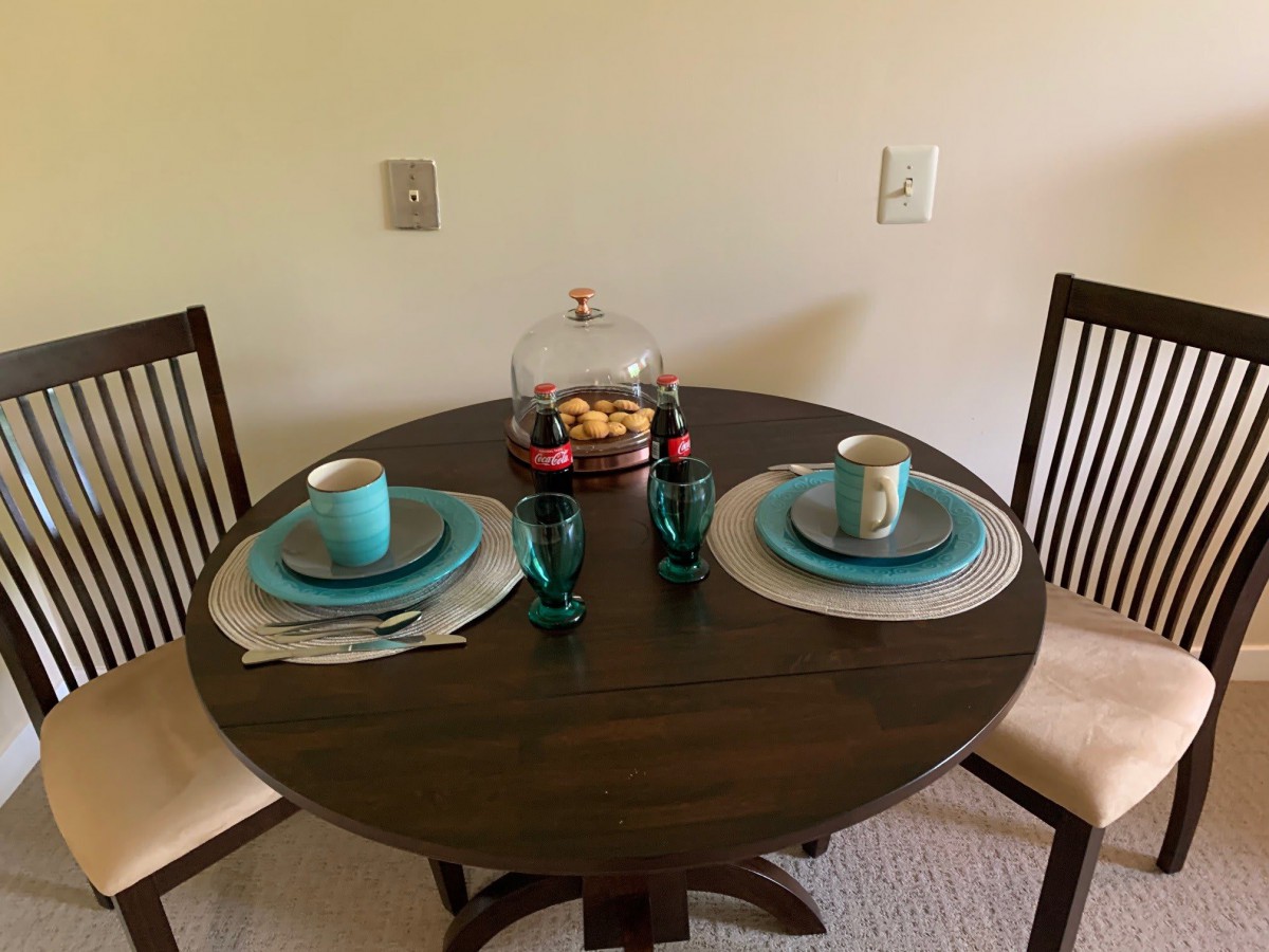 A small round dining table set for two with turquoise dinnerware and glasses, featuring a decorative glass dome filled with candies.