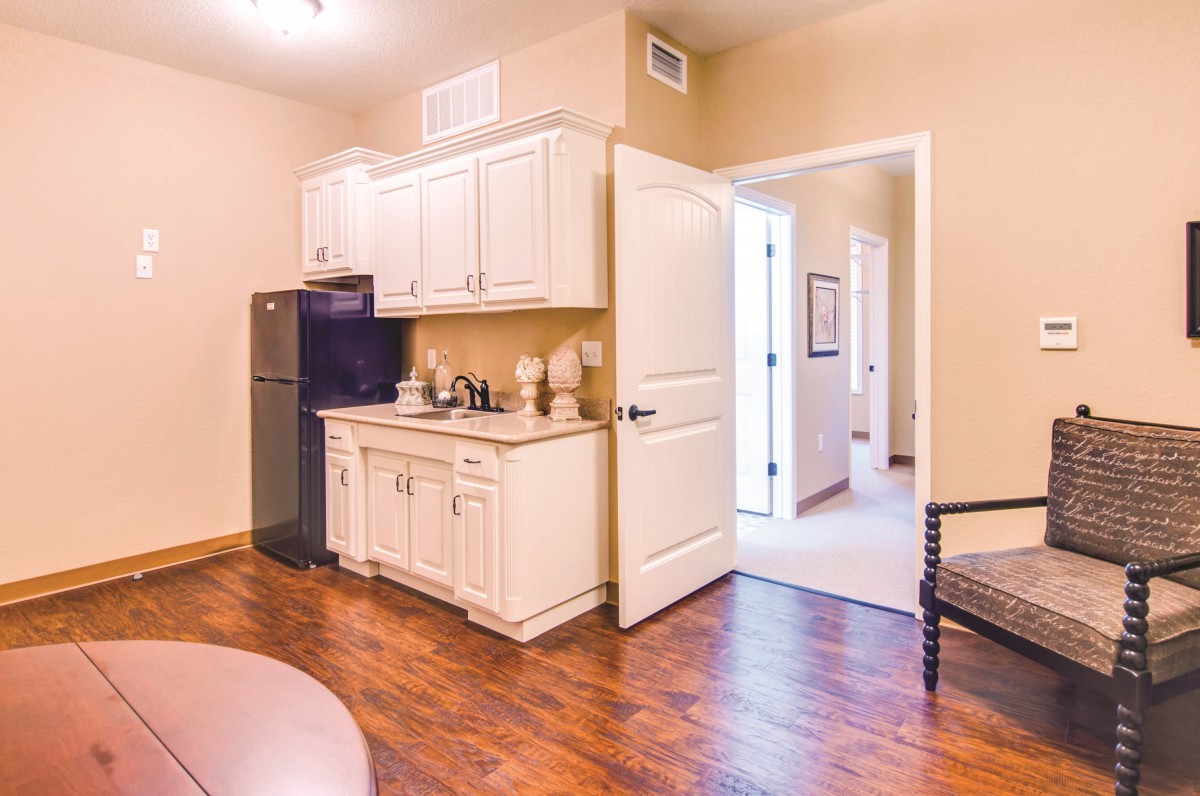 A cozy kitchen area with white cabinets, a small fridge, and hardwood floors.