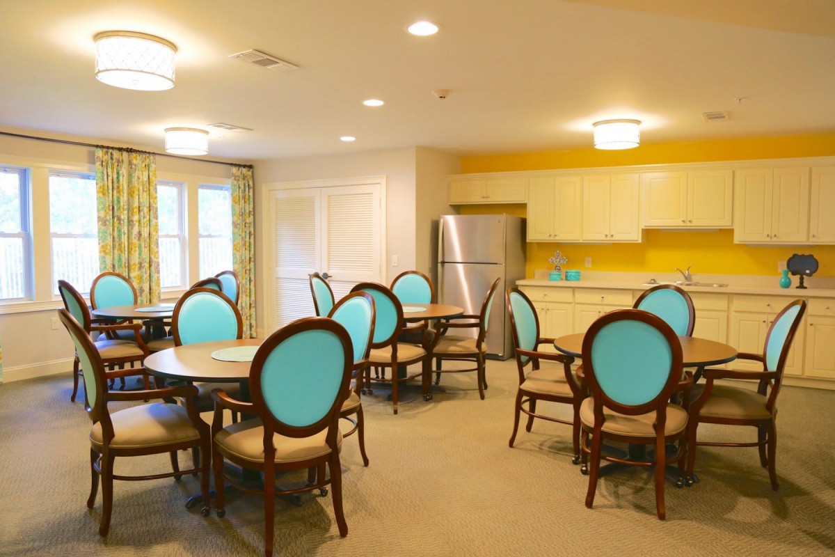 A brightly colored dining room with teal-backed chairs and a connected kitchen area.