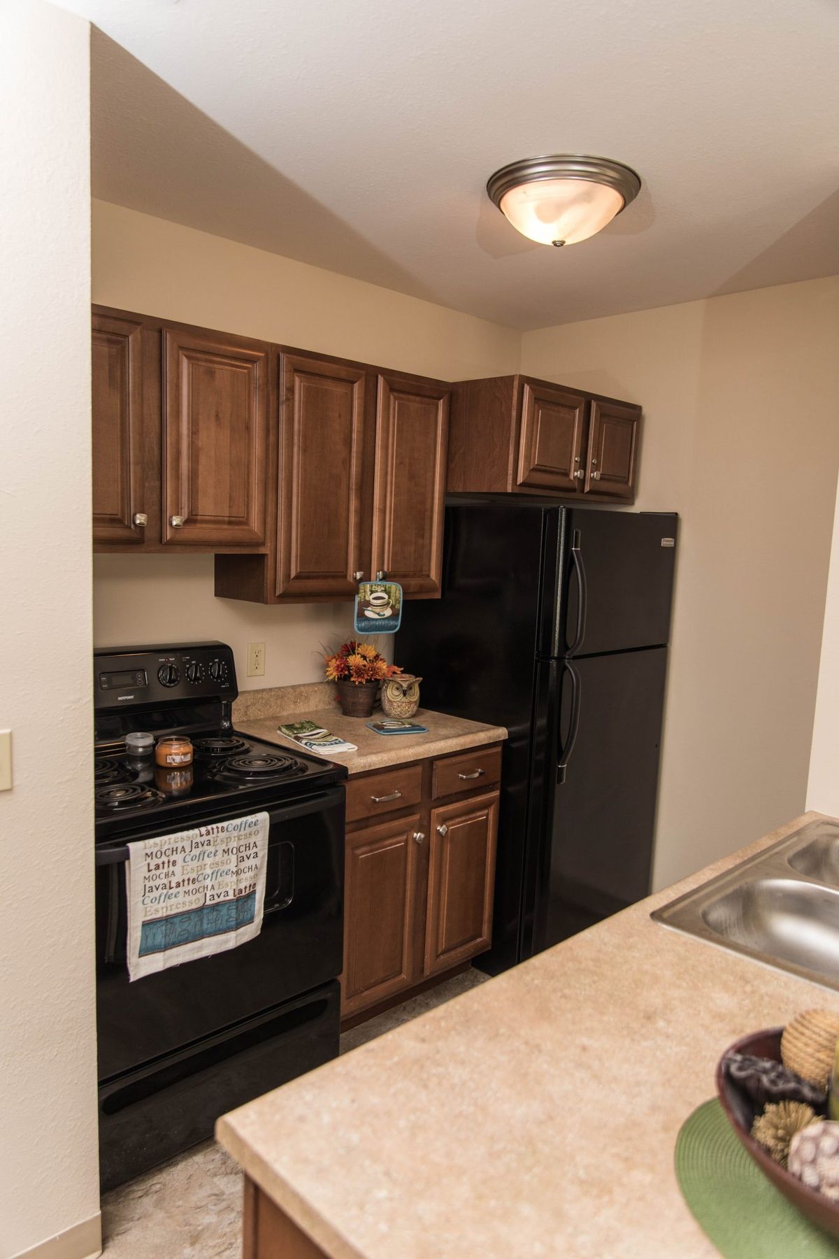 A compact apartment kitchen with wooden cabinets, a stove, and a refrigerator.