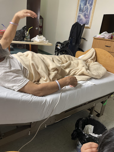 A patient resting in a hospital bed, covered with a blanket and connected to medical equipment.