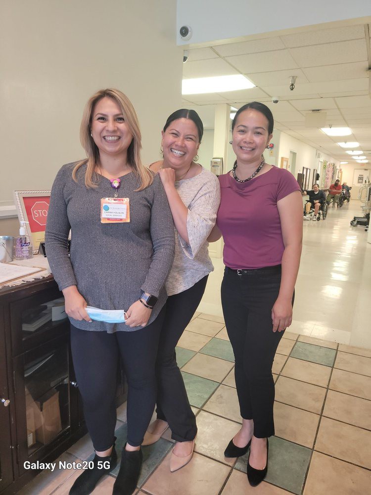 Three women smiling and posing together in a hallway, likely in a hospital or clinic setting.