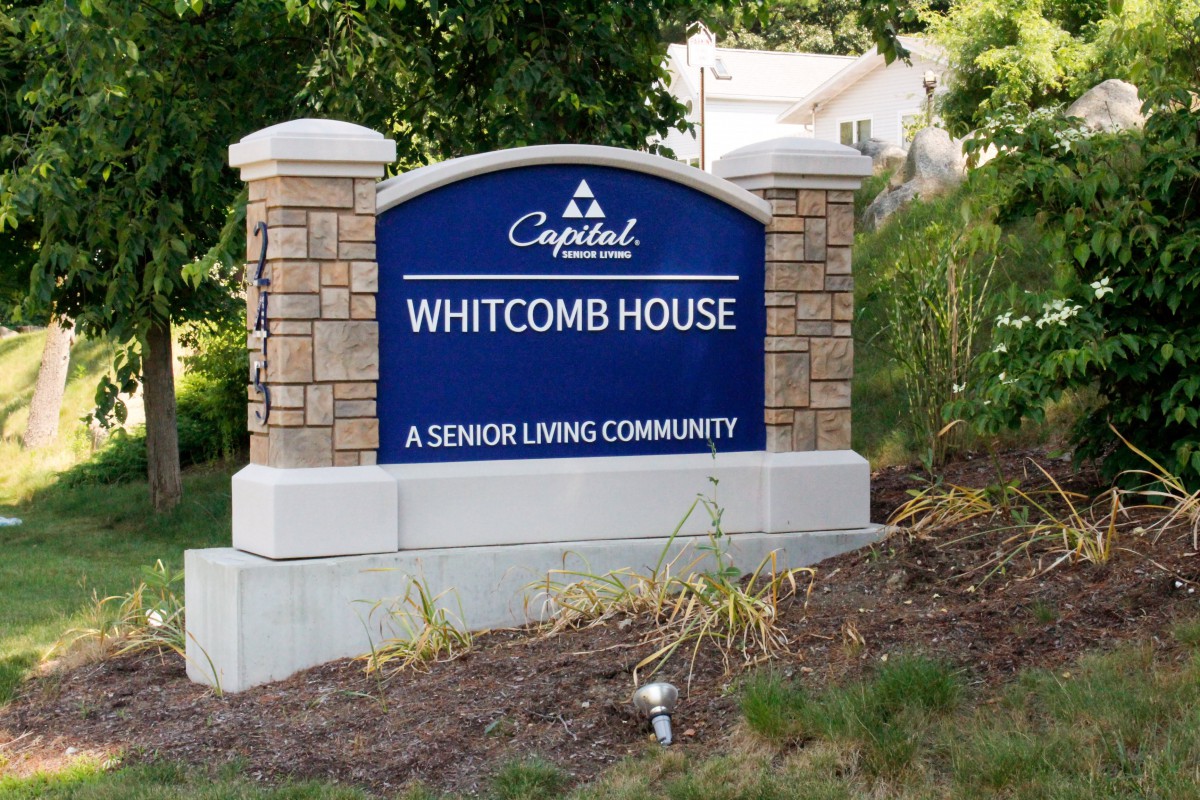 A sign for Whitcomb House, a senior living community, surrounded by landscaping.