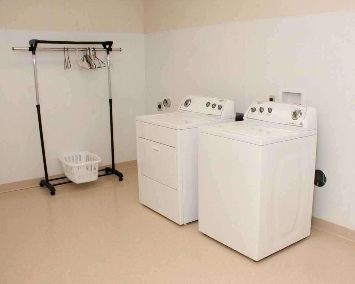 A tidy laundry room featuring a washing machine, dryer, clothes rack with hangers, and a laundry basket.