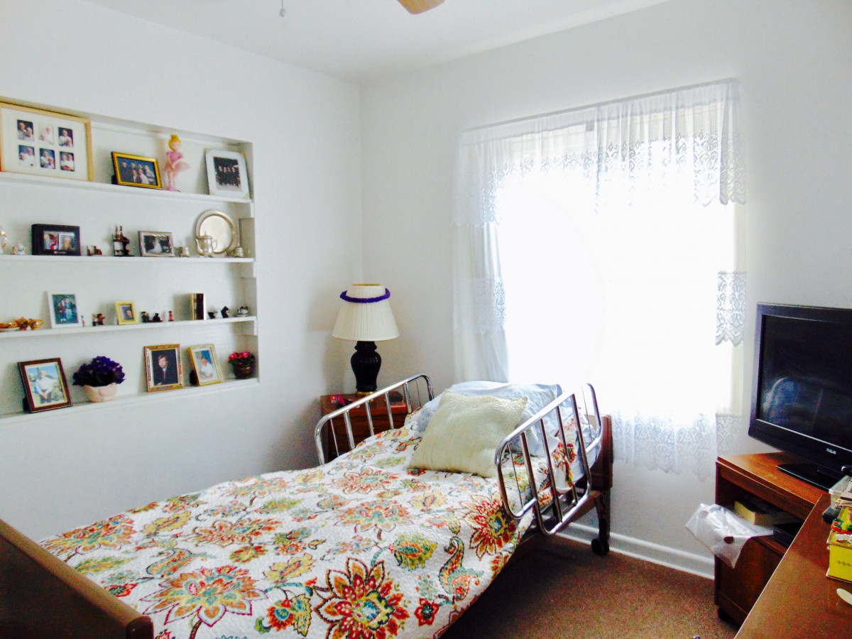 A cozy bedroom with a single bed, decorated shelves, and a window letting in natural light.