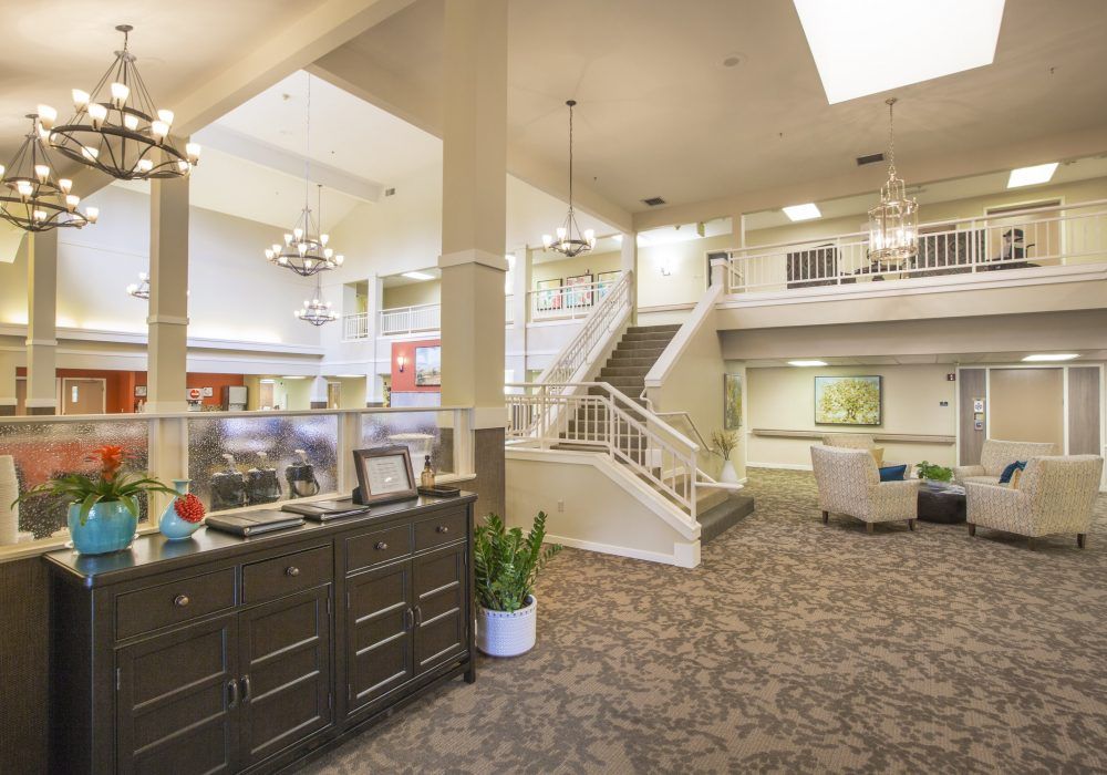 A spacious and well-lit lobby area with a grand staircase, stylish furniture, and elegant chandeliers.