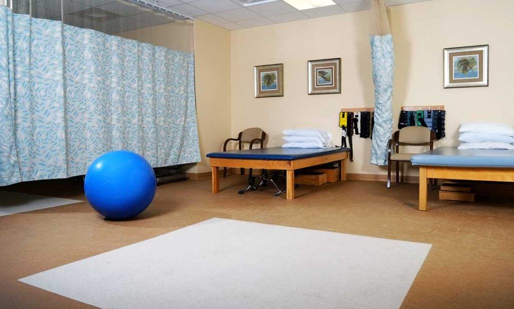 A physical therapy room with a treatment table, exercise equipment, and chairs.