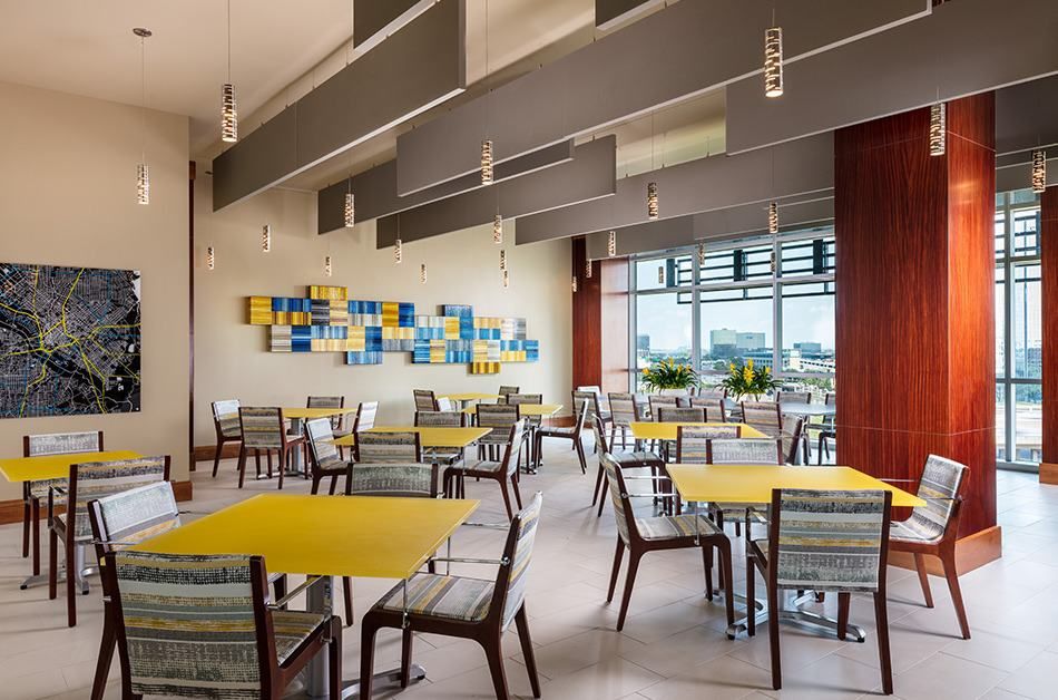 A modern cafeteria interior with yellow tables and colorful artwork on the wall.