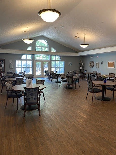 A spacious dining area with several tables and chairs, featuring large windows and wooden flooring.