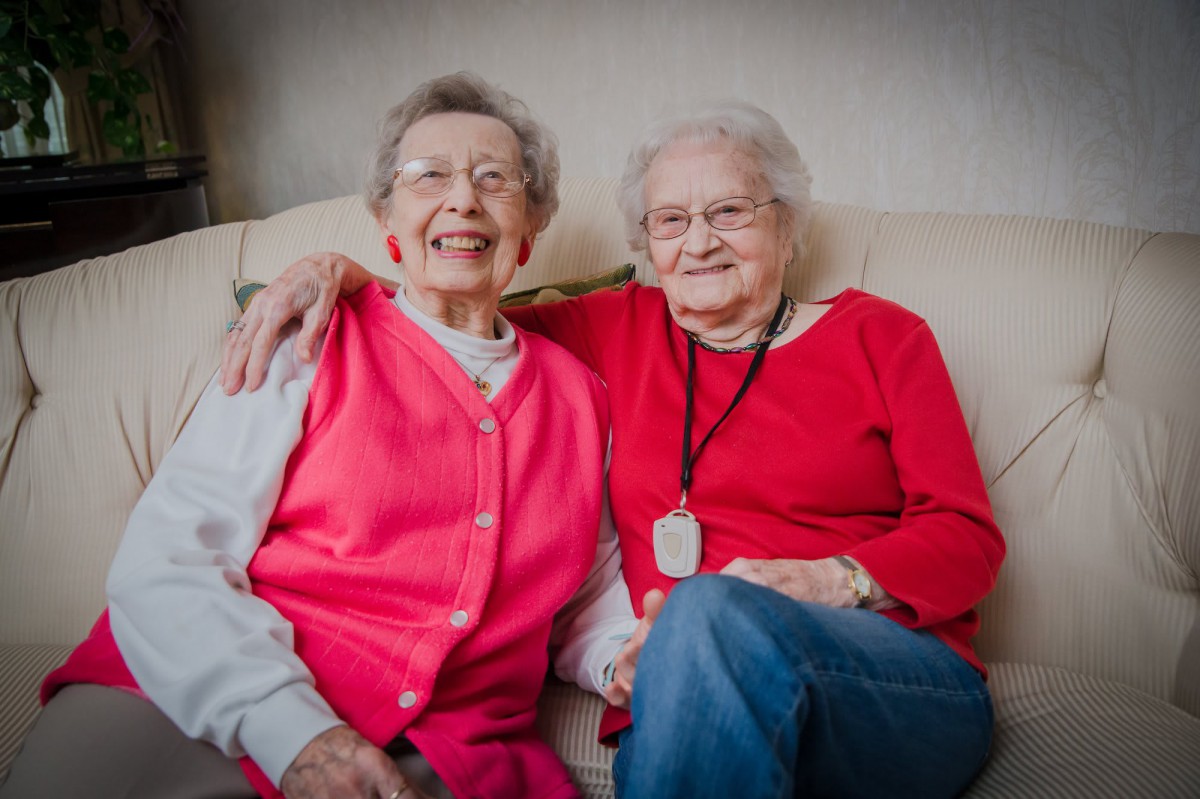 Two elderly women sitting together on a couch, smiling and enjoying each other's company.