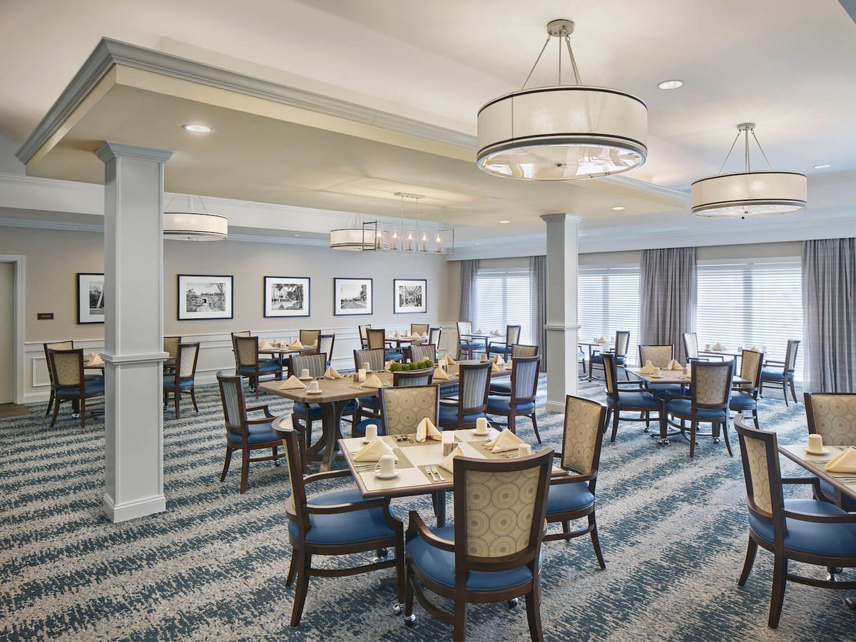 An elegant dining space with neatly arranged tables and chairs, illuminated by chandeliers.