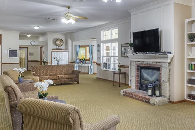 A cozy living room with sofas, a television above the fireplace, and ample natural light through the windows.