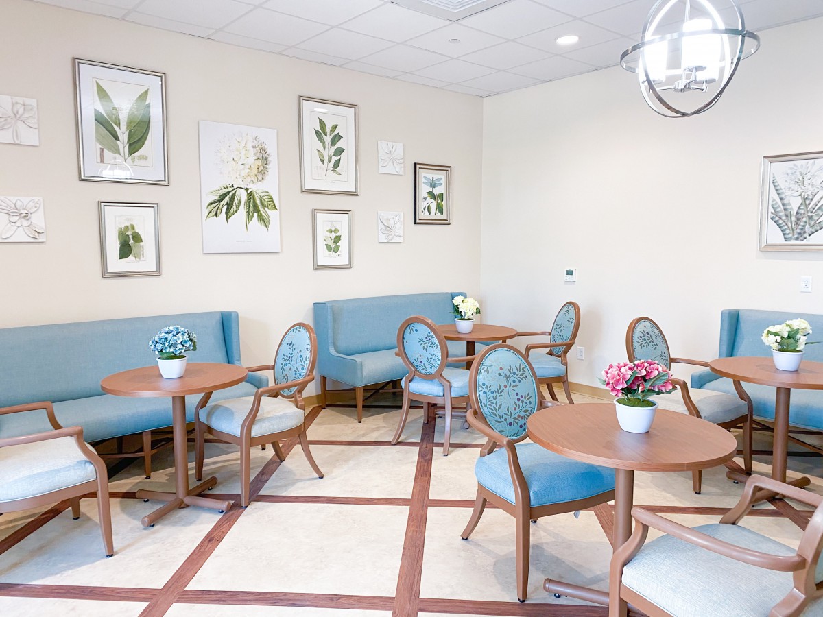 A modern waiting room with blue seating, wooden tables, botanical artwork, and potted plants.