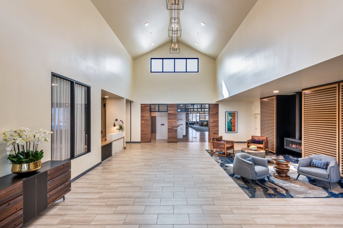 A modern and spacious lobby with a high ceiling, featuring comfortable seating and wood flooring.