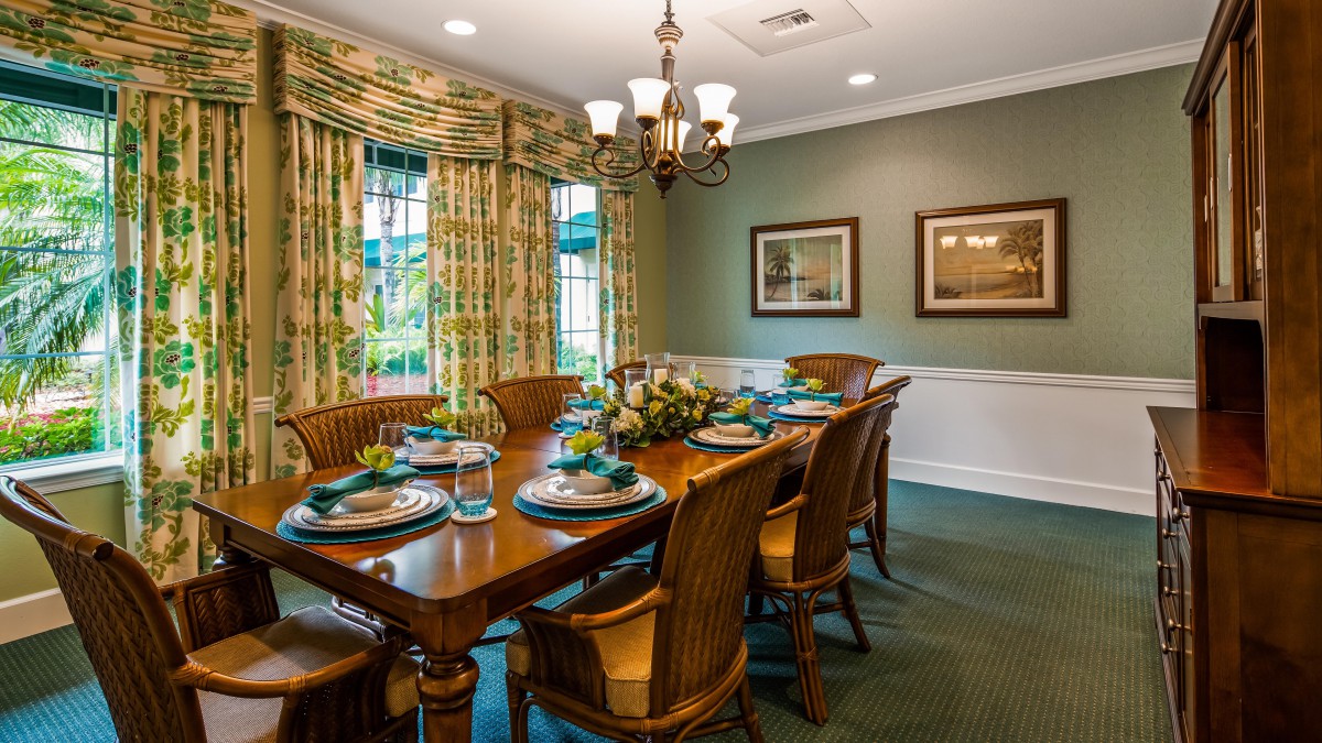 A warmly decorated dining room with a wooden table set for a meal, surrounded by chairs and lit by an elegant chandelier.