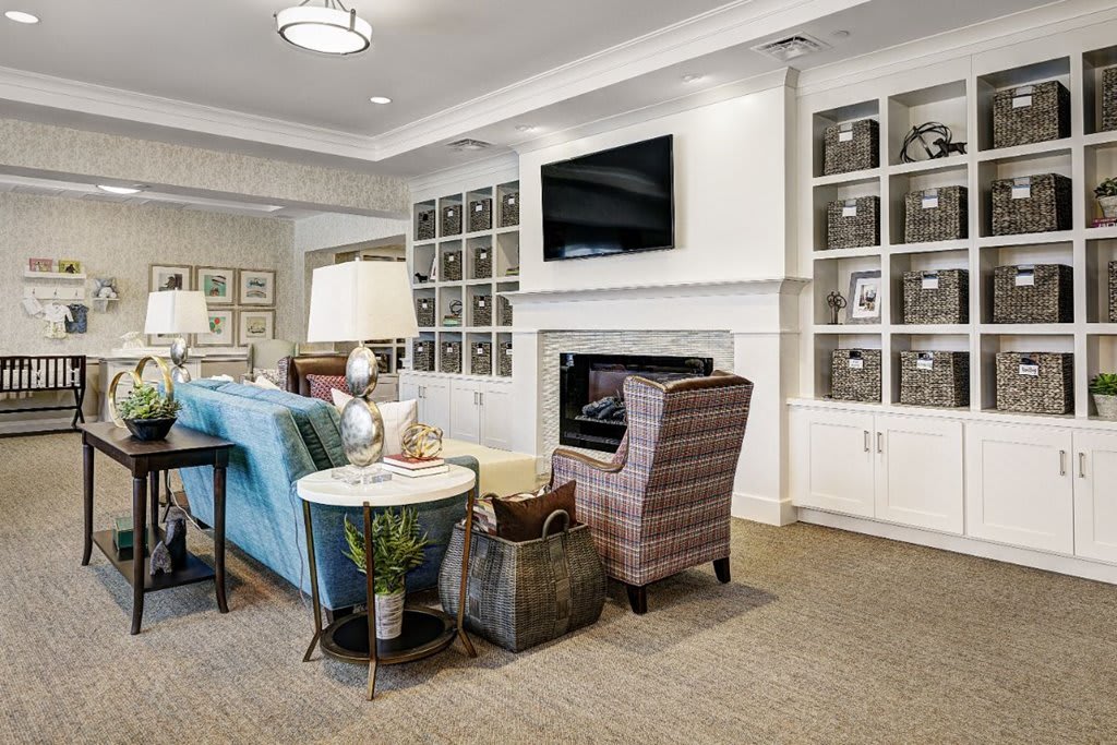 A cozy living room featuring comfortable seating, a television above the fireplace, and neatly organized shelves.