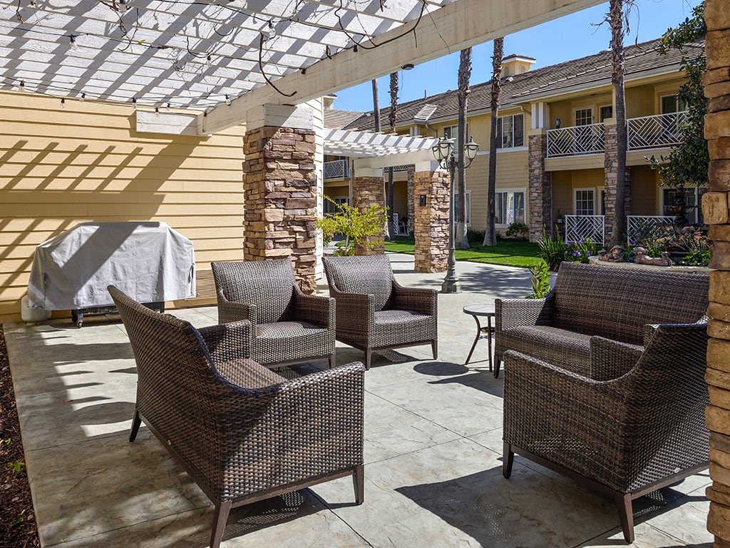 An outdoor patio area with wicker chairs and a table under a pergola in an apartment complex.