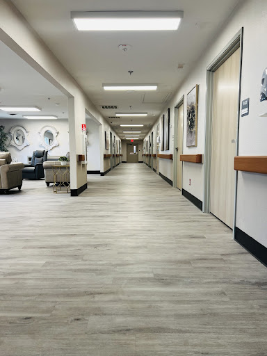 A view of a well-lit hallway in a healthcare facility, featuring seating areas and doors along the sides.