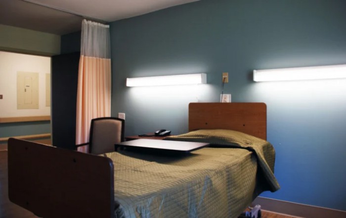 A hospital room with a single bed and overhead lighting.