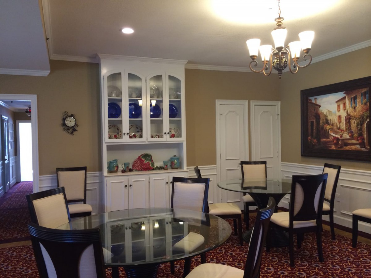 A well-decorated dining room featuring glass tables, upholstered chairs, a chandelier, and built-in cabinetry displaying decorative items.