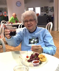 An elderly woman raises a glass while enjoying a meal at a restaurant.
