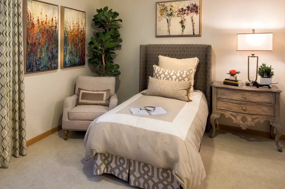 A cozy bedroom with a single bed, decorative pillows, an armchair, and artwork on the walls.