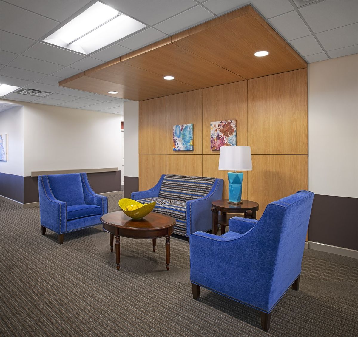 A modern lobby area featuring blue upholstered chairs, a sofa, and a small table with a lamp.