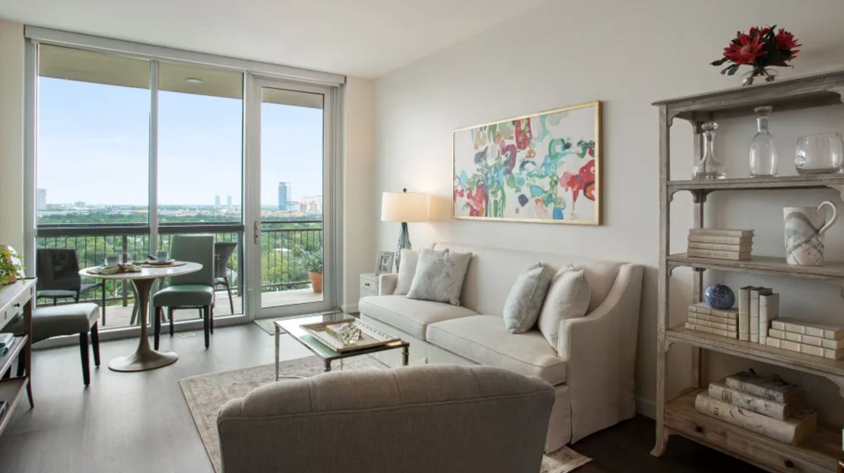 A modern living room with stylish decor, featuring a comfortable sofa, coffee table, and large artwork, opening to a balcony with a city view.