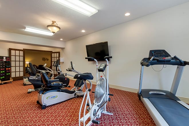 A compact fitness room featuring a treadmill, stationary bikes, and a television.