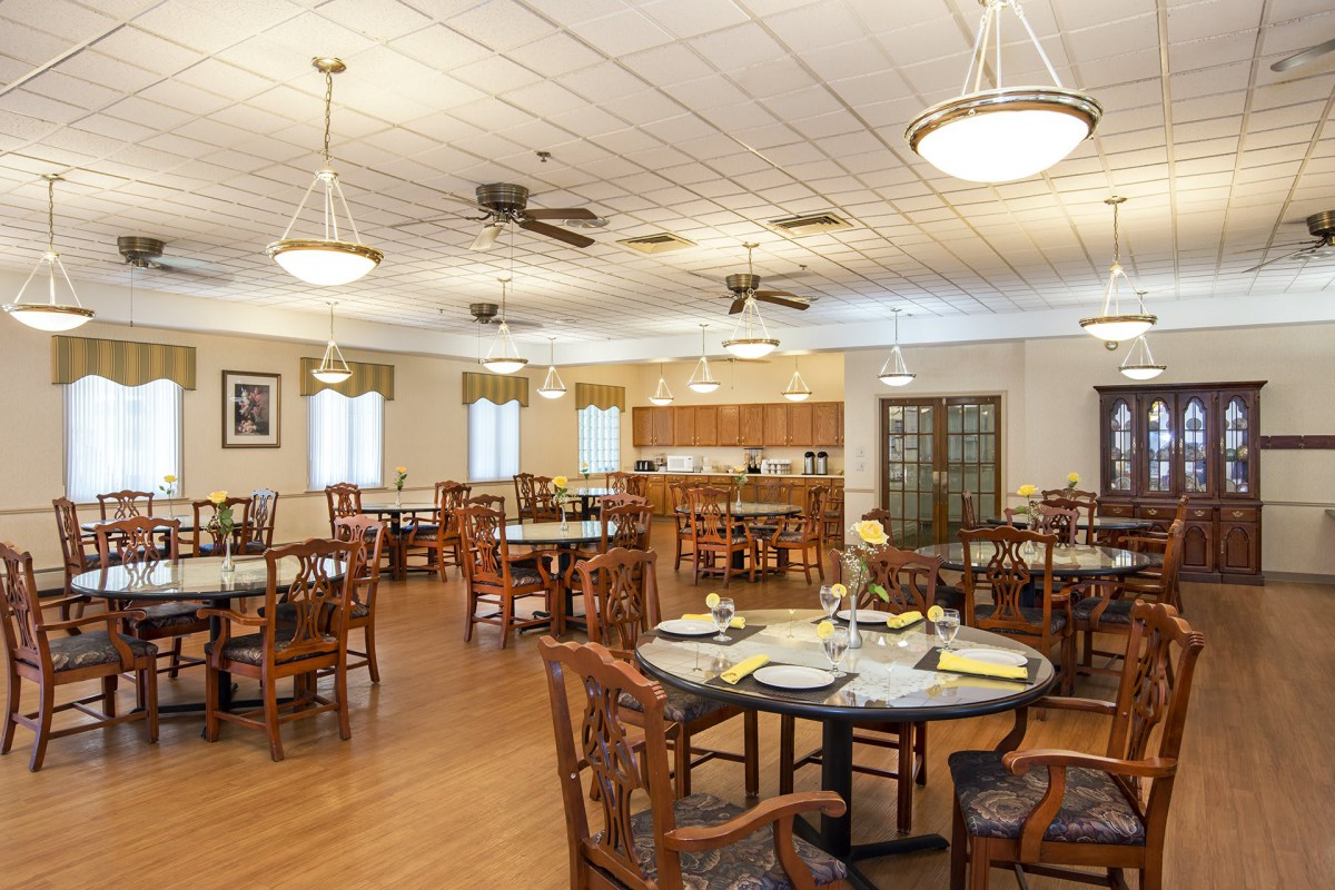 A spacious dining room with neatly arranged tables and chairs, featuring elegant lighting and wooden flooring.