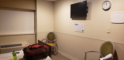 A simple hospital room featuring a bed, a television mounted on the wall, and a chair.