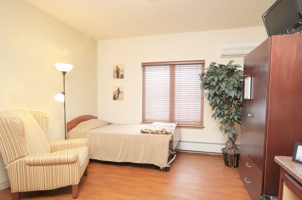 A cozy bedroom featuring a bed, striped armchair, floor lamp, and a large plant by the window.