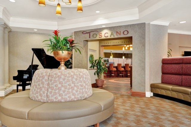 A stylish lobby with a seating area, featuring a piano and the entrance to a restaurant named Toscano.