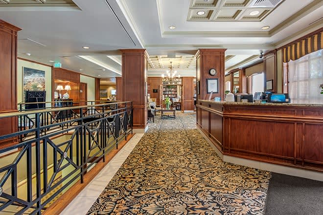 A luxurious hotel lobby featuring a reception desk, elegant carpeting, and a chandelier.