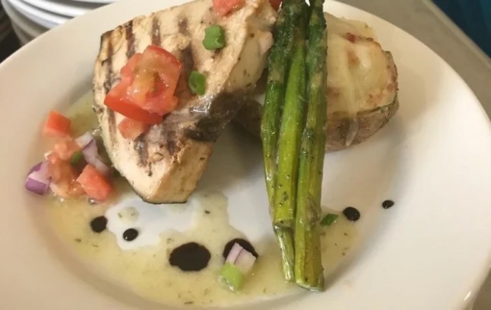 A gourmet dish featuring grilled fish topped with tomato garnish and served with asparagus and a drizzle of balsamic glaze.