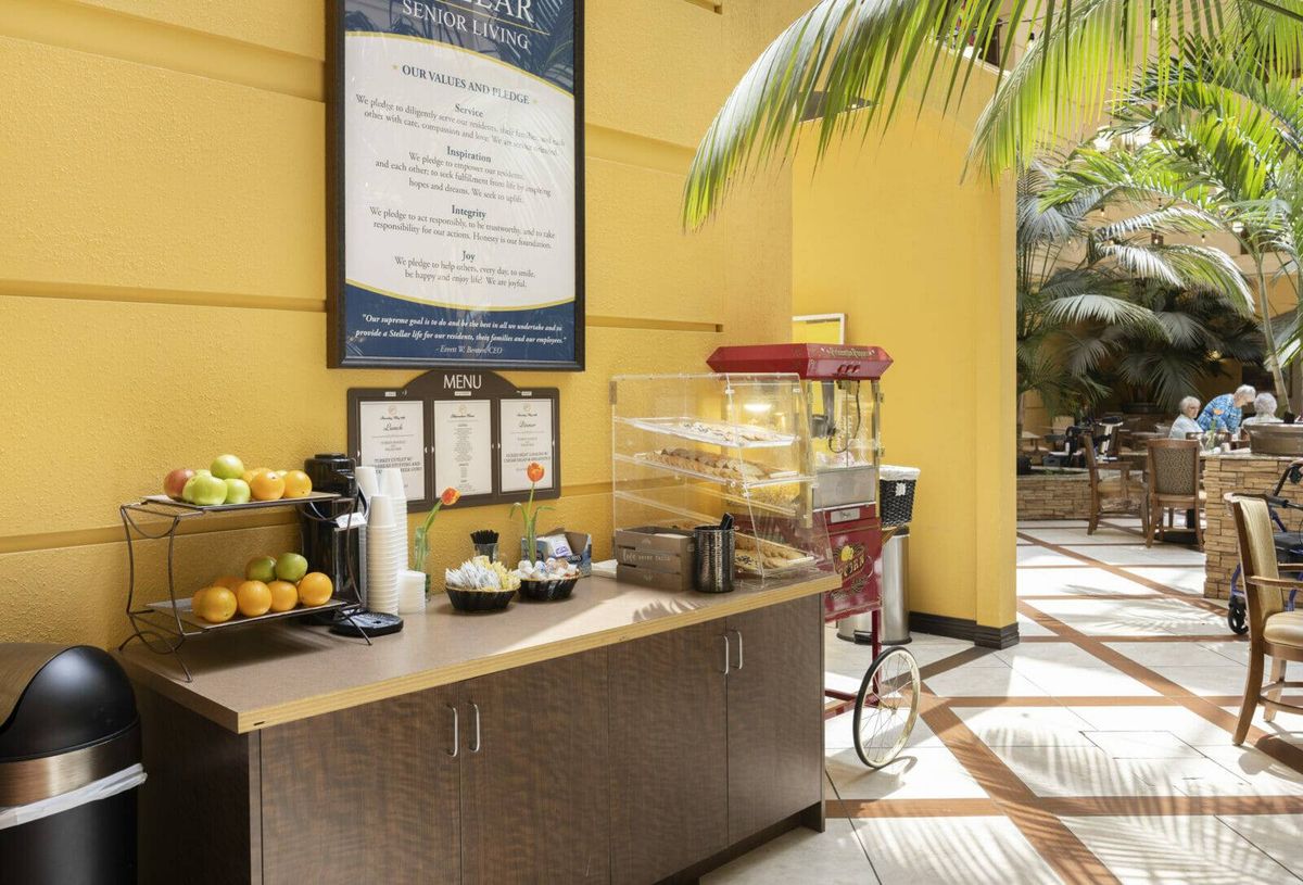 A cozy refreshment area featuring a popcorn machine, fresh fruits, and a coffee station against a vibrant yellow wall.