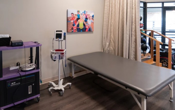 A medical clinic room featuring a treatment table, medical equipment, and artwork on the wall.