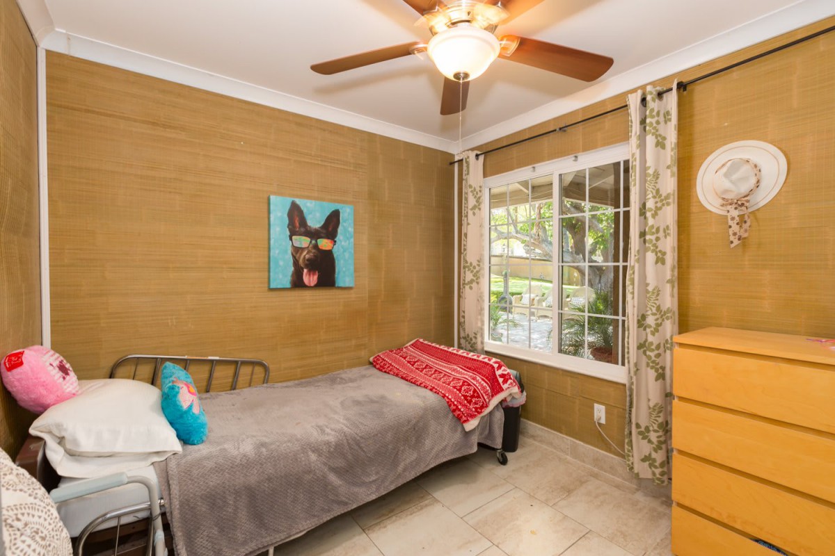 A cozy bedroom with a single bed, featuring a dog painting and a ceiling fan.