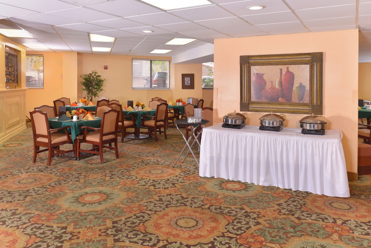 A spacious dining area with a buffet setup, featuring elegantly arranged tables and chairs on a patterned carpet.