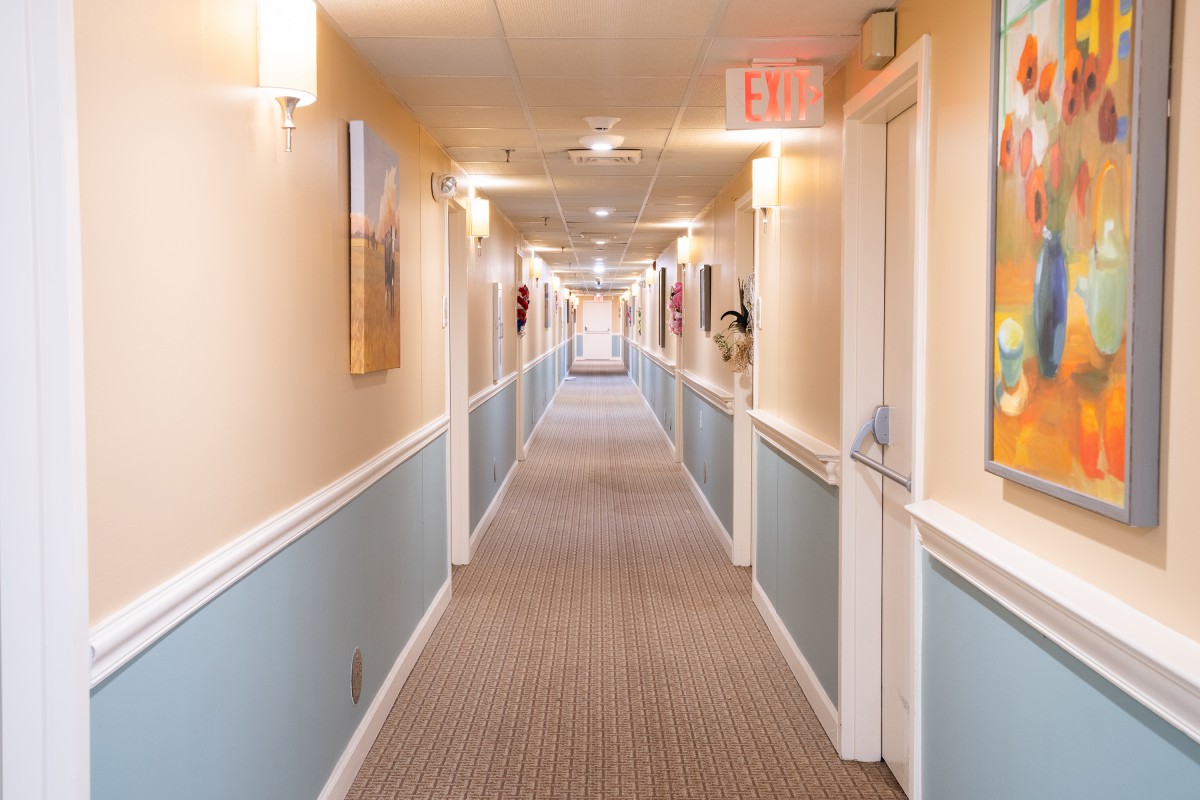 A long, carpeted hallway with doors on both sides and overhead lighting.