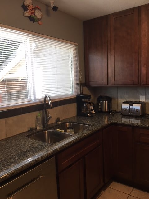 A modern kitchen with granite countertops, wooden cabinets, and various appliances near a window with blinds.