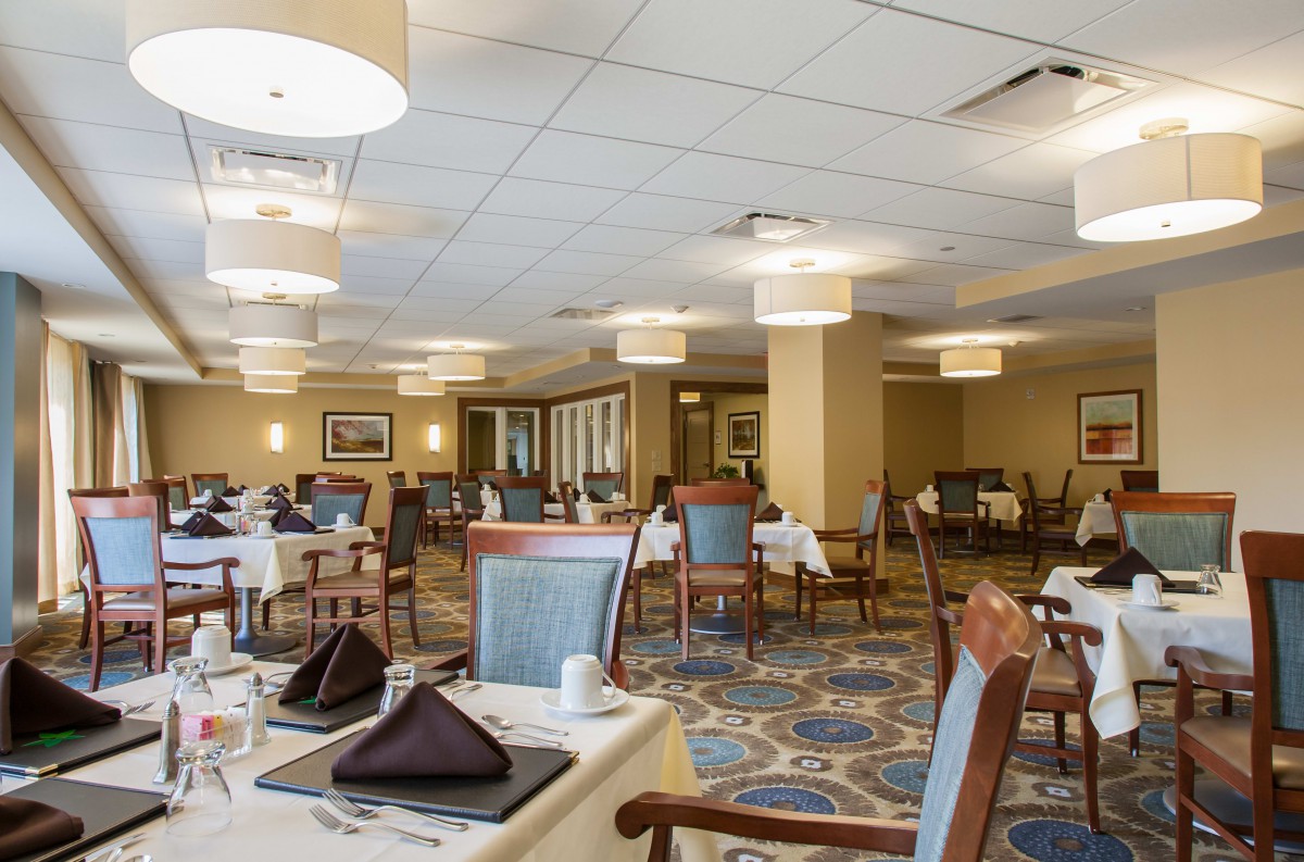 An elegantly furnished dining area with neatly arranged tables and chairs, softly lit by overhead lights.