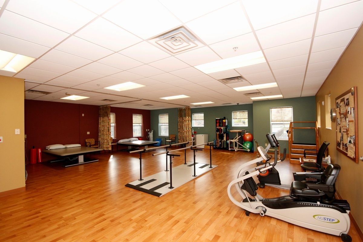 A spacious gym with various exercise equipment and wooden flooring.